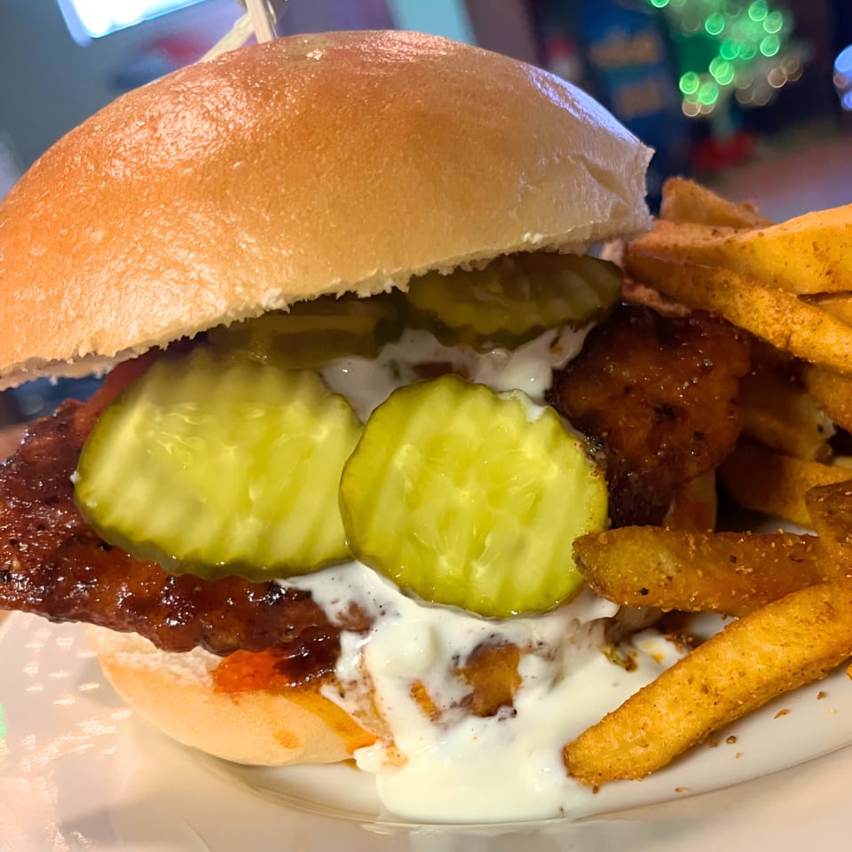 A Southwood Bar burger with pickles, white sauce, and a side of fries on a white plate.