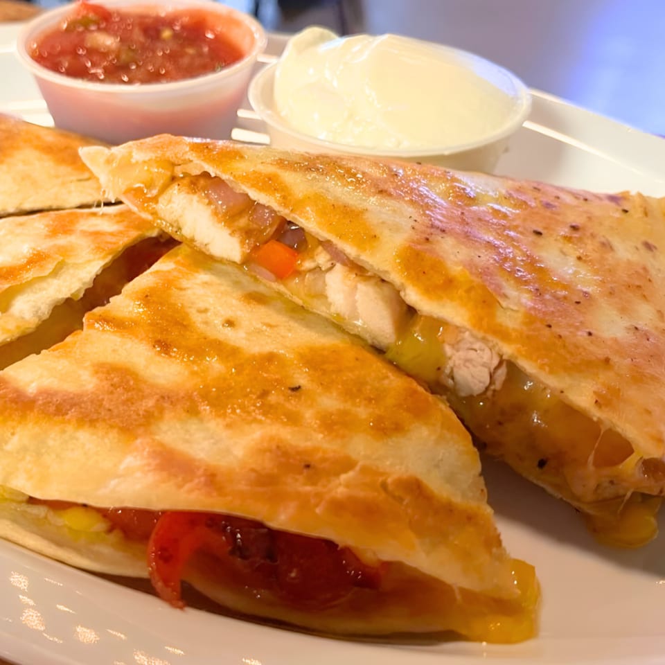 Golden-brown chicken quesadillas with melted cheese, salsa, and sour cream on a white plate.
