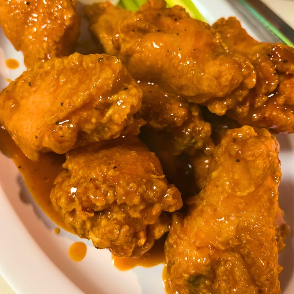 Close-up of Southwood Bar's buffalo chicken wings, glistening with orange sauce and black pepper.