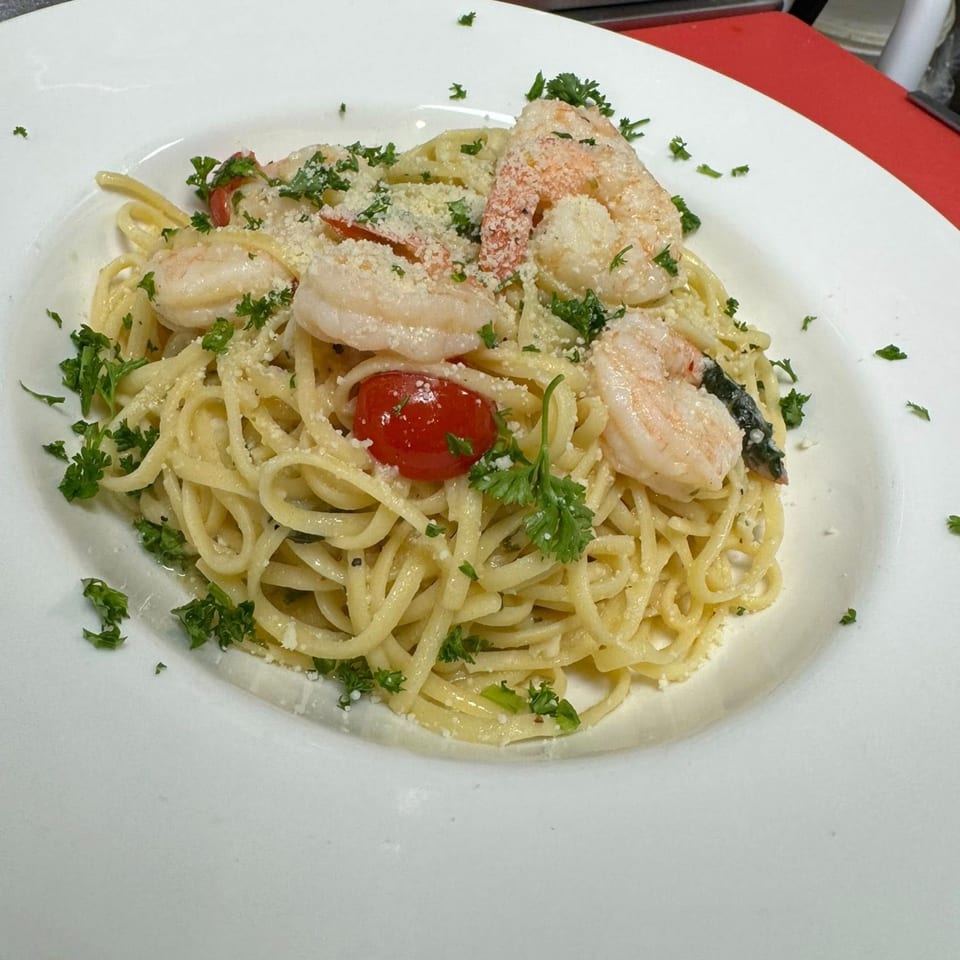 Shrimp scampi with linguine, cherry tomatoes, parmesan, and parsley on a white plate.