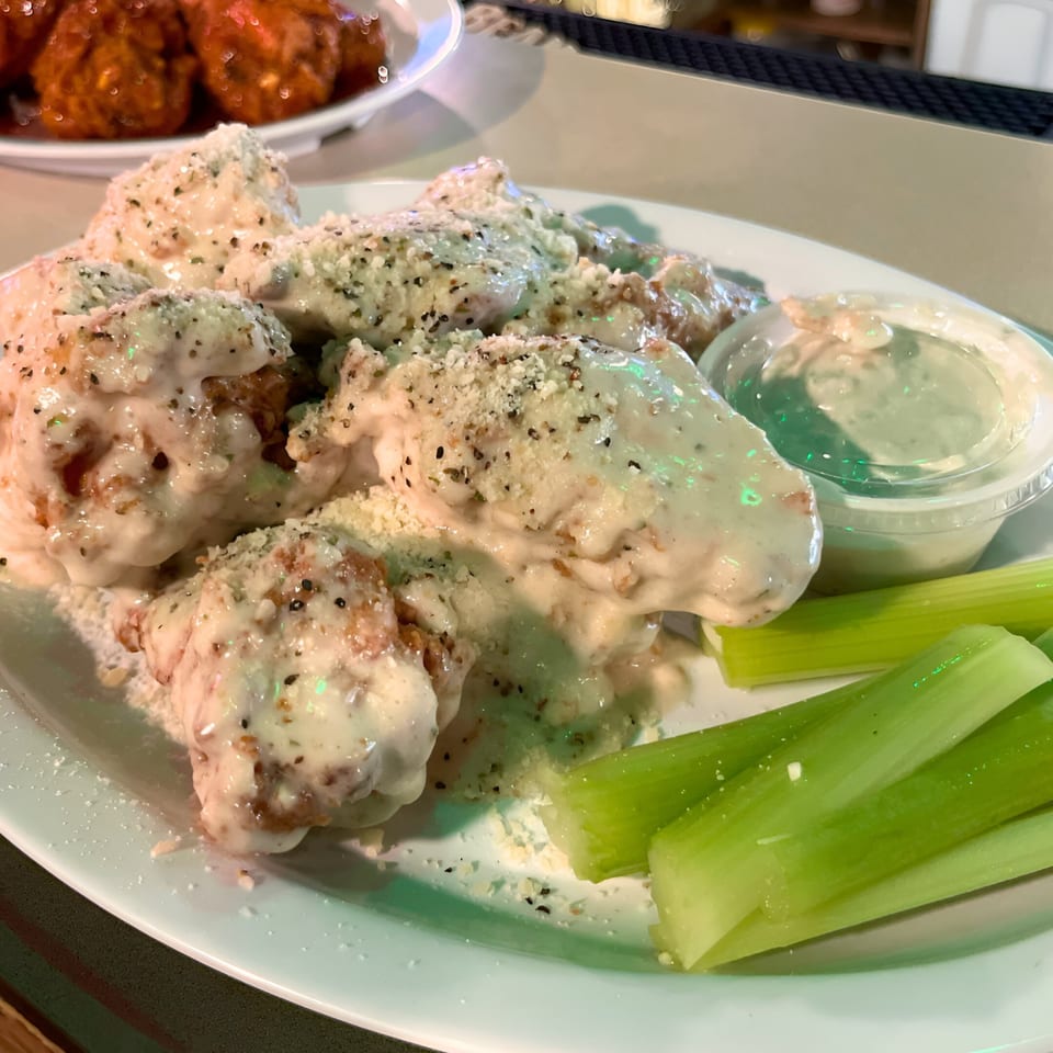 Garlic Parmesan wings with celery sticks and a side of ranch dressing on a white plate.